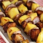 Four pineapple chicken kabobs with metal skewers on a white plate