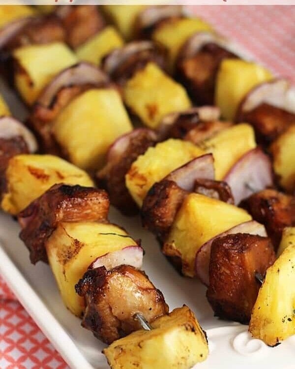 Four pineapple chicken kabobs with metal skewers on a white plate