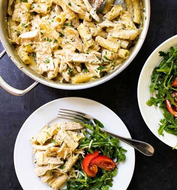 Creamy pesto chicken pasta in a pot and on a white plate with salad