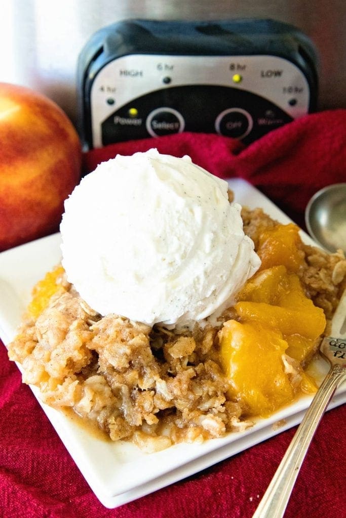 Crock Pot Peach crisp dished up onto a white plate, topped with a dollop of ice cream.