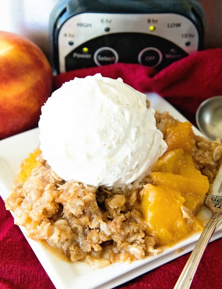 Crock Pot Peach Cobbler with ice cream on white plate in front of crock pot