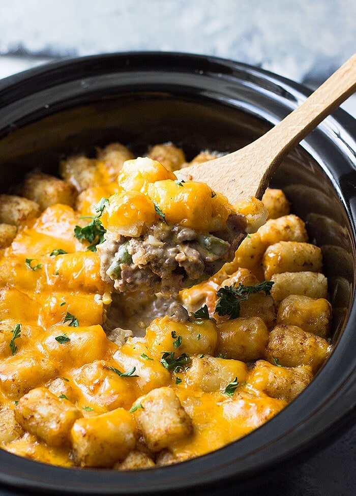 Wooden spoon scooping Tater Tot Casserole from Crock Pot