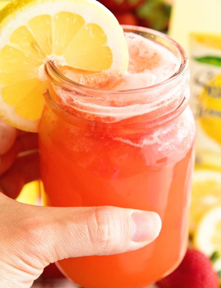 hand holding mason jar full of sparkling strawberry lemonade with a lemon slice