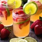 Three mason jars of strawberry limeade sangria with strawberries and limes slices in the glasses and on the counter