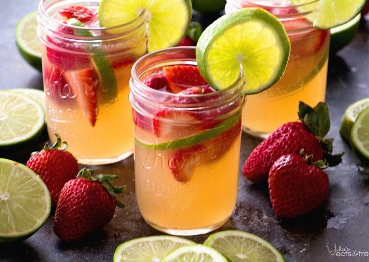 Three mason jars of strawberry limeade sangria with strawberries and limes slices in the glasses and on the counter