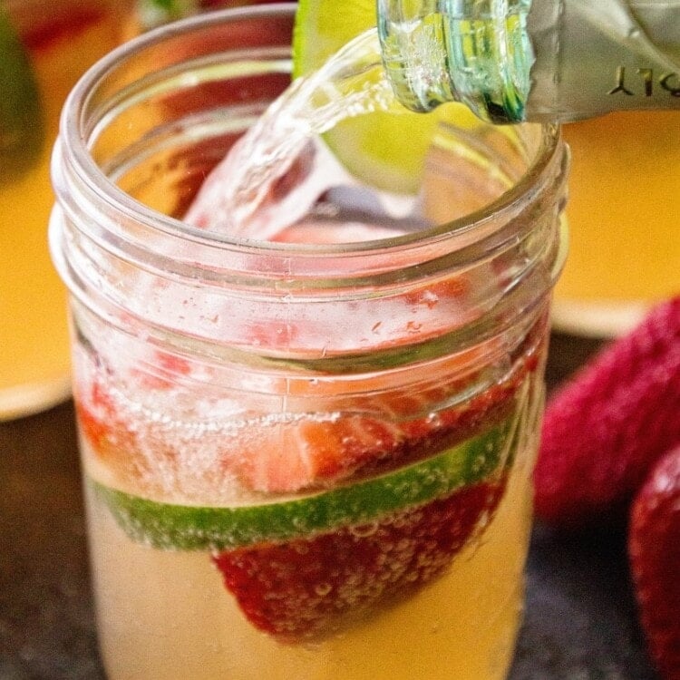 Strawberry Limeade Sangria in small mason jar with bottle pouring champagne into glass