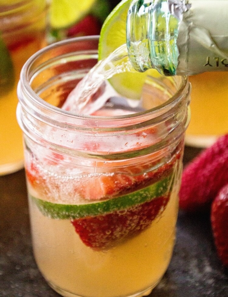 Strawberry Limeade Sangria in small mason jar with bottle pouring champagne into glass