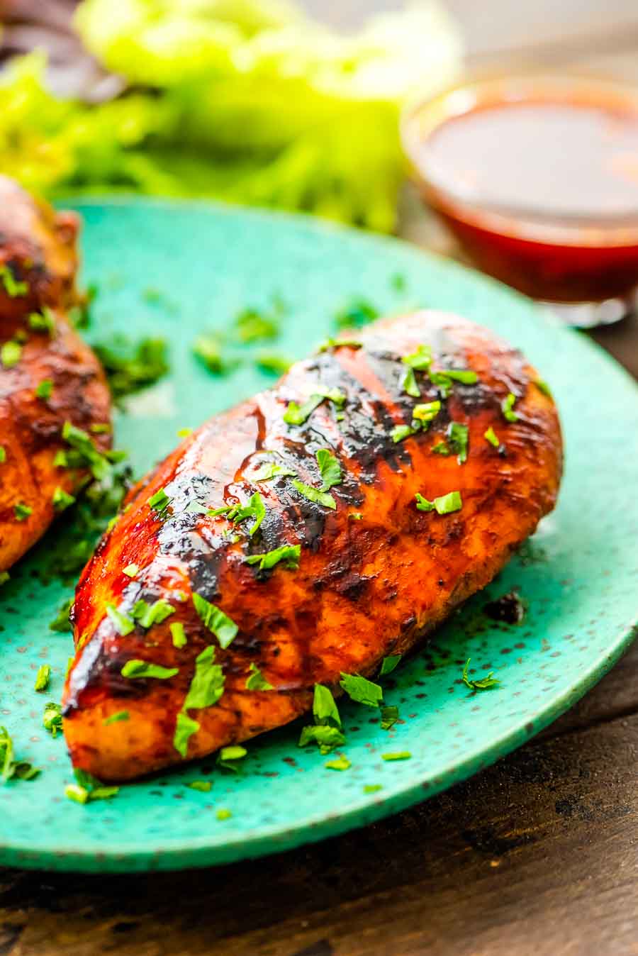 BBQ Chicken on green plate with a dish of BBQ Marinade in small glass bowl in background