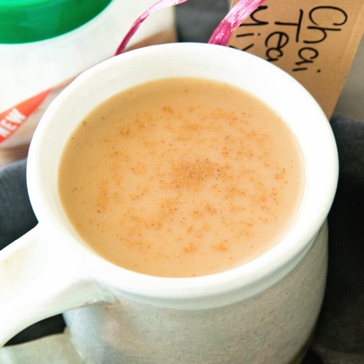 A white mug of chai tea next to a jar of chai tea mix, a container of splenda, and some cinnamon sticks