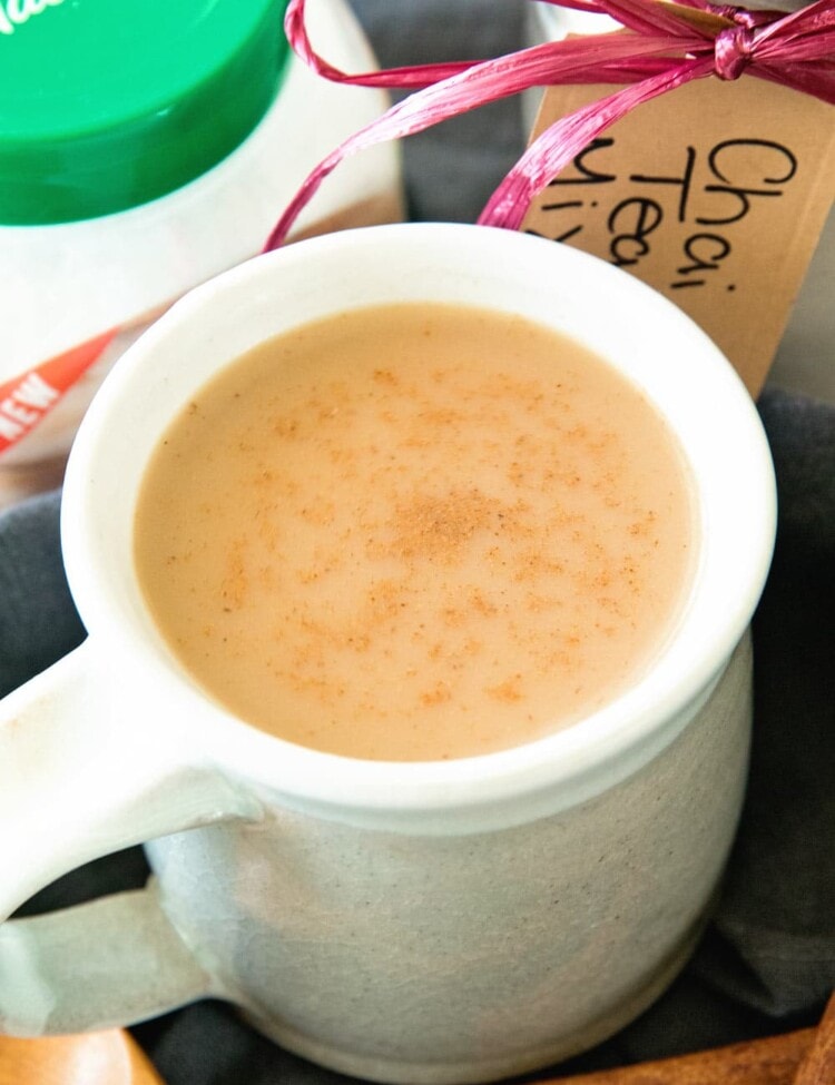 A white mug of chai tea next to a jar of chai tea mix, a container of splenda, and some cinnamon sticks