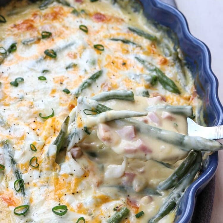 Green bean and ham casserole in a blue baking dish with a spoon