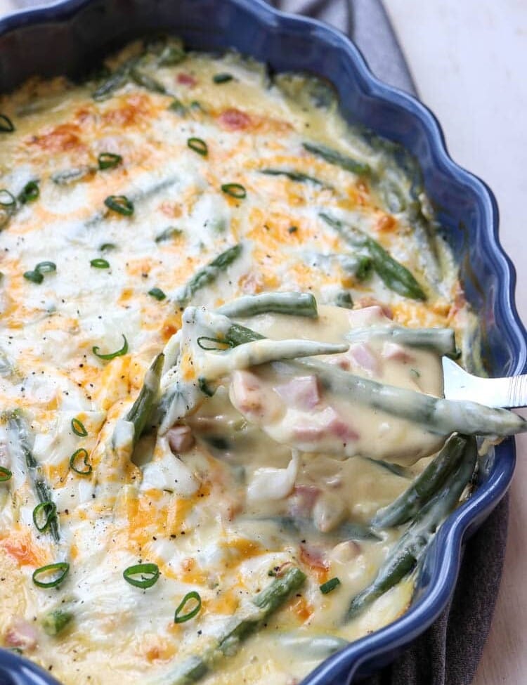 Green beans and ham casserole in a blue baking dish with a spoon scooping some out