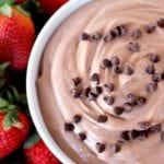 A white bowl of healthy chocolate fruit dip with mini chocolate chips surrounded by oranges, strawberries, and apple slices