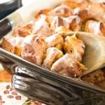 Pumpkin cinnamon roll bake in a square baking dish with a wooden spoon scooping some out