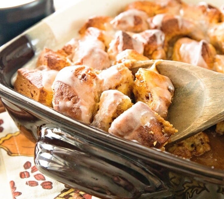 Pumpkin cinnamon roll bake in a square baking dish with a wooden spoon scooping some out