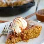 Slice of pumpkin snickerdoodle cookie from a skillet topped with a scoop of vanilla ice cream and caramel sauce on a white plate with a fork