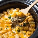 Wooden spoon scooping bacon cheeseburger tater tot casserole out of a crock pot