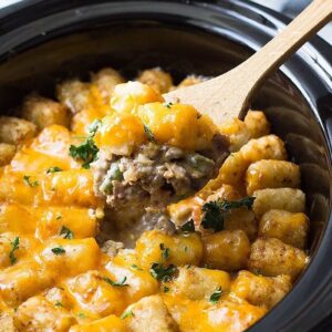 Wooden spoon scooping bacon cheeseburger tater tot casserole out of a crock pot