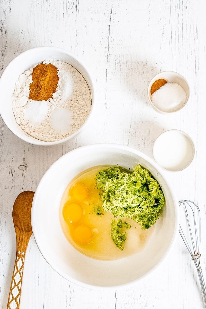 Bowl with eggs and shredded zucchini in it with more ingredients in small bowls next to it