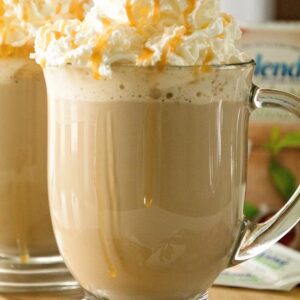 Glass mug of caramel latte with whipped cream topping and caramel drizzle