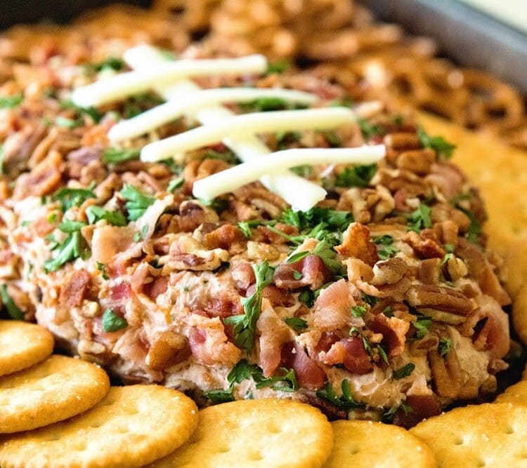 Cheesy bacon ranch football shaped cheese ball surrounded by ritz crackers and pretzels
