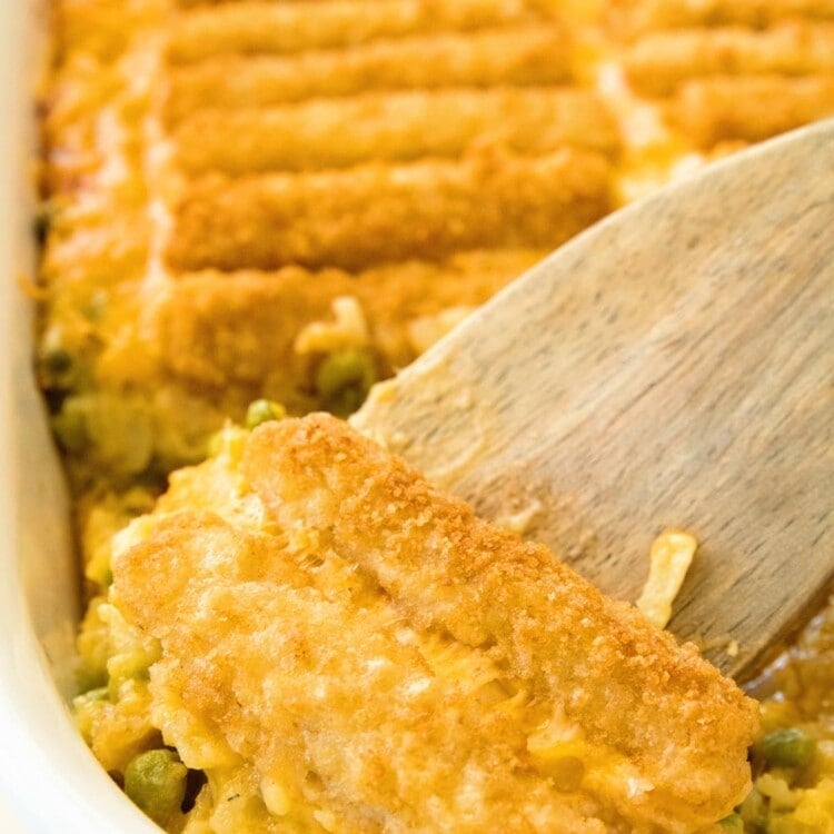 Cheesy Fish Stick Hash Brown Casserole in a white baking dish with a wood spatula