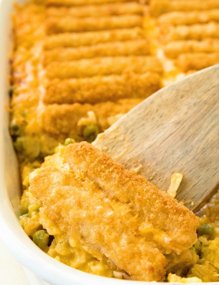 Cheesy Fish Stick Hash Brown Casserole in a white baking dish with a wood spatula