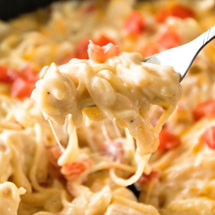 A bite of mexican spaghetti on a fork over a skillet of cheesy mexican spaghetti