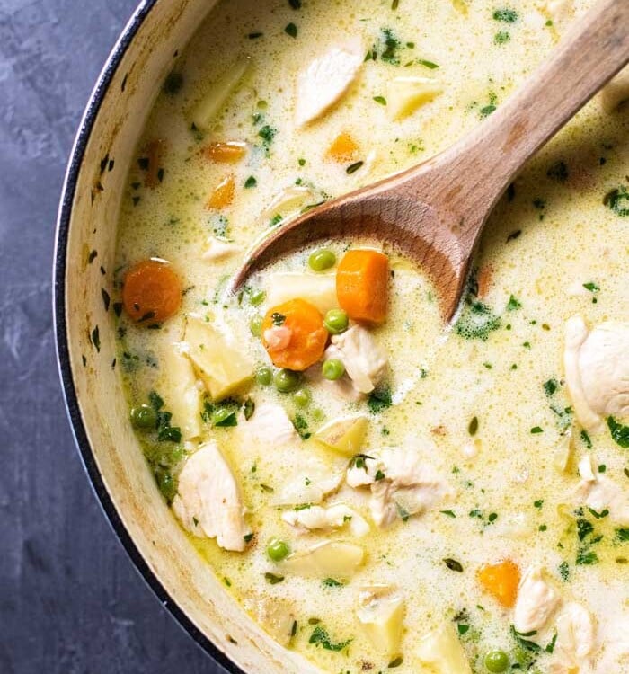 Chicken pot pie soup in a pot with a wooden spoon
