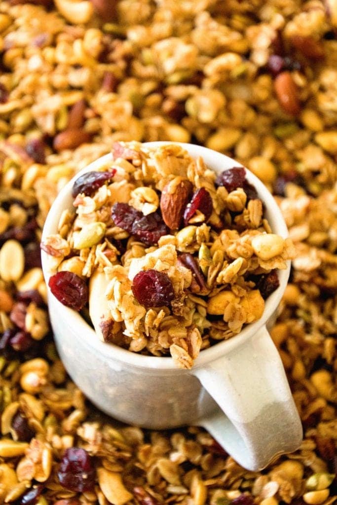 Off white mug full of pumpkin granola sitting in a pan filled with more granola.