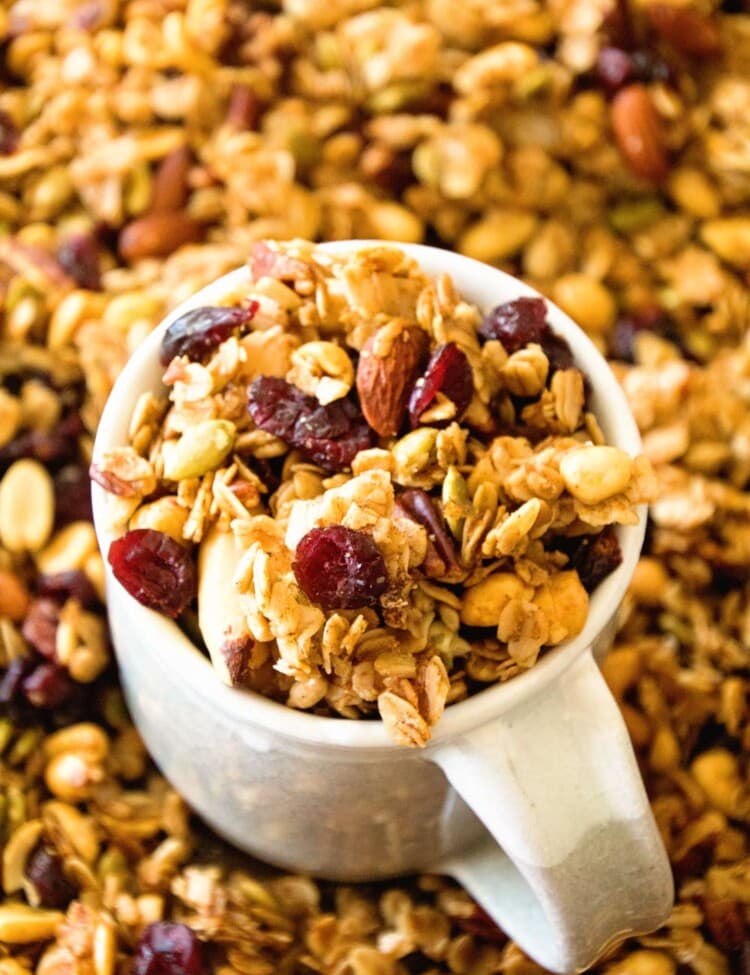 Pumpkin granola in a white mug sitting in a pile of pumpkin spice granola