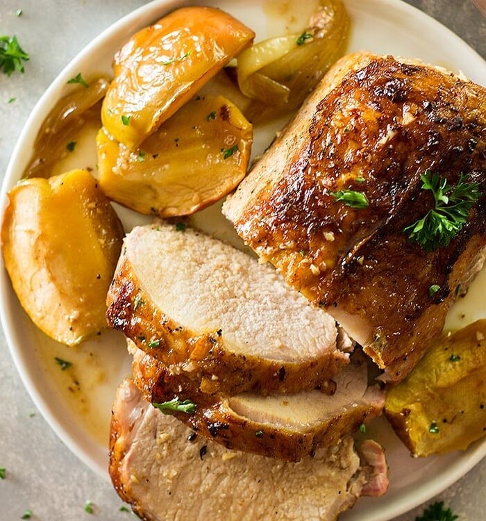 A partially slice pork loin on a cream plate with cooked apple slices