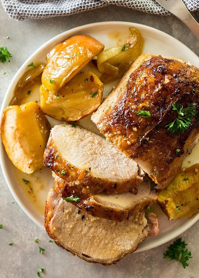 A partially slice pork loin on a cream plate with cooked apple slices