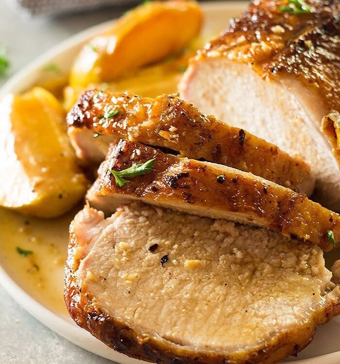 Slices of maple pork roast with apples and onions on the side on a white plate