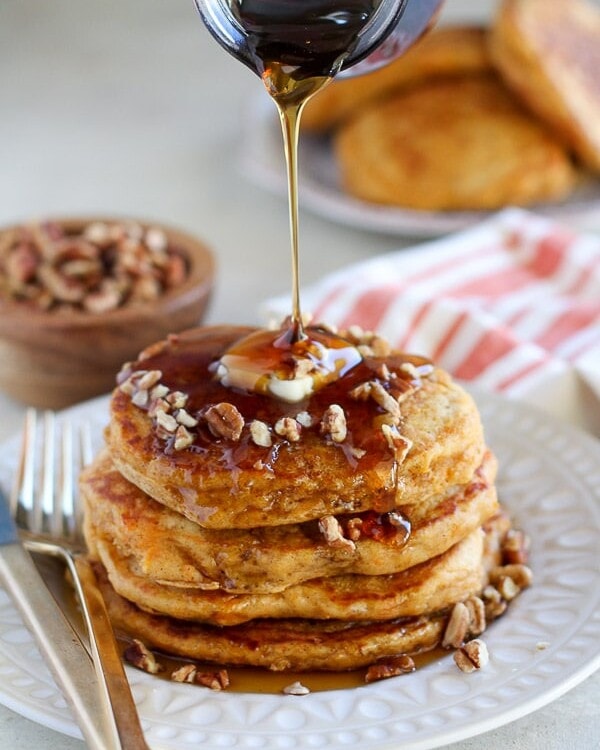 A stack of sweet potato pancakes with syrup being poured over the top