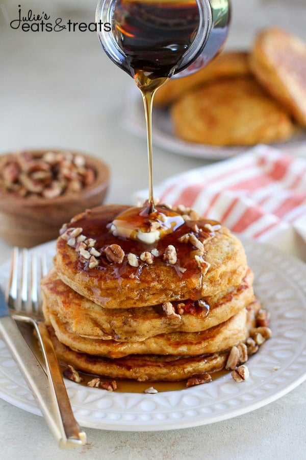 Syrup being poured over stack of sweet potato pancakes on a white dish.