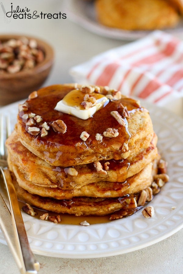 White plate with stack of sweet potato pancakes that are topped with chopped nuts, butter and syrup.