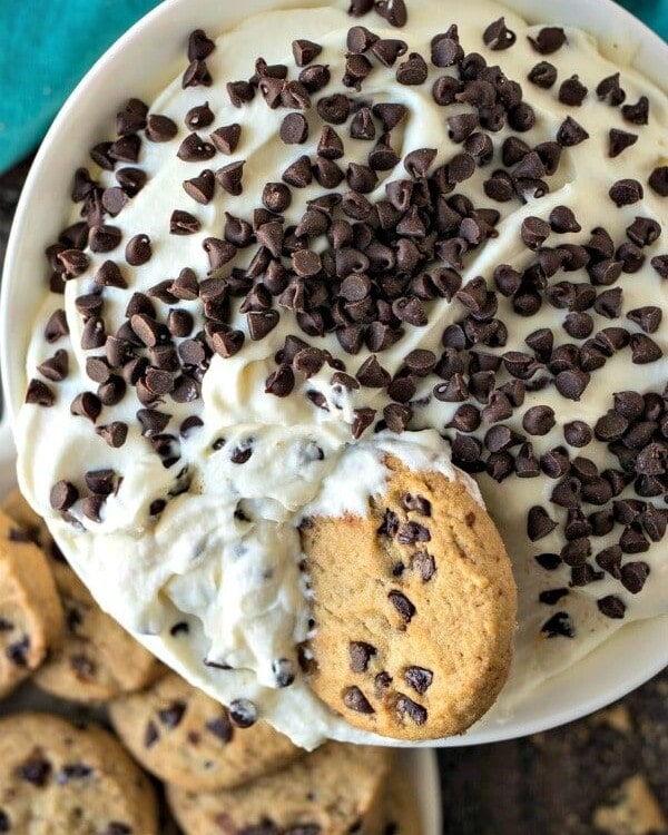 White bowl of cannoli dip with chocolate chips cookies in it and on a plate next to it