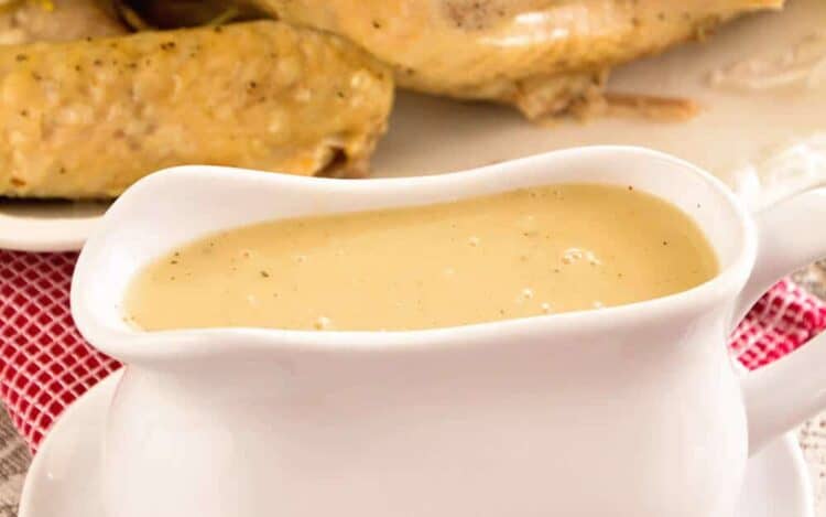 A white gravy boat of easy homemade gravy in front of a cooked turkey