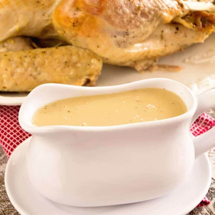 A white gravy boat of easy homemade gravy in front of a cooked turkey