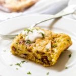 Piece of green chile breakfast enchilada casserole with sour cream on a white plate with a fork