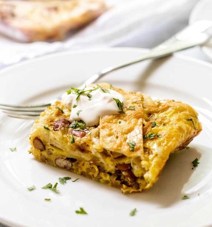 Piece of green chile breakfast enchilada casserole with sour cream on a white plate with a fork