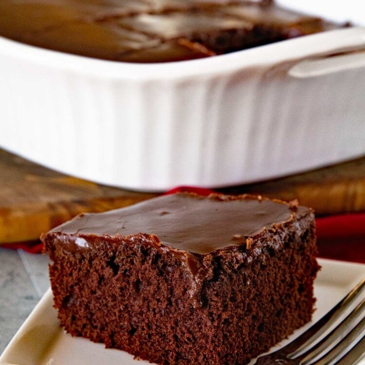 A slice of chocolate cake with chocolate frosting on a square white plate with a fork
