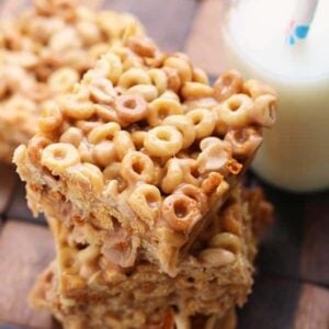 Astack of no bake cheerio peanut butter bars on a wood board with a glass of milk