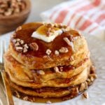 Stack of sweet potato pancakes with butter, syrup, and chopped pecans on a white plate with a fork