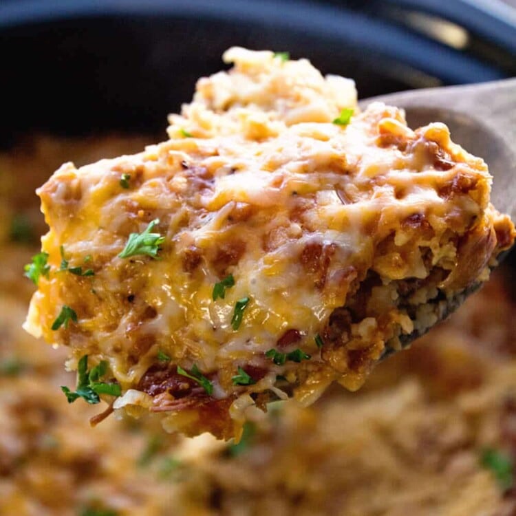 Scoop of turkey breakfast casserole on a wooden spoon being held over a black crock pot of casserole