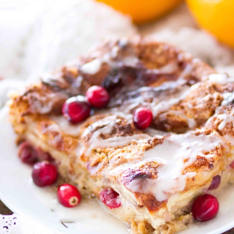 Large piece of cranberry orange bread pudding on a white plate with icing and cranberries