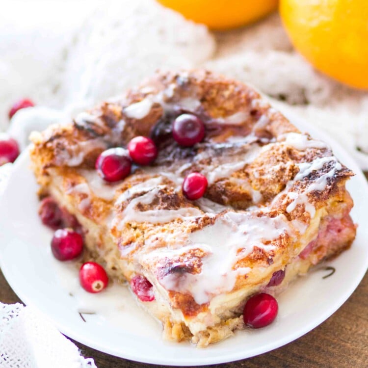 A large slice of cranberry orange bread pudding topped with icing on a white plate with cranberries