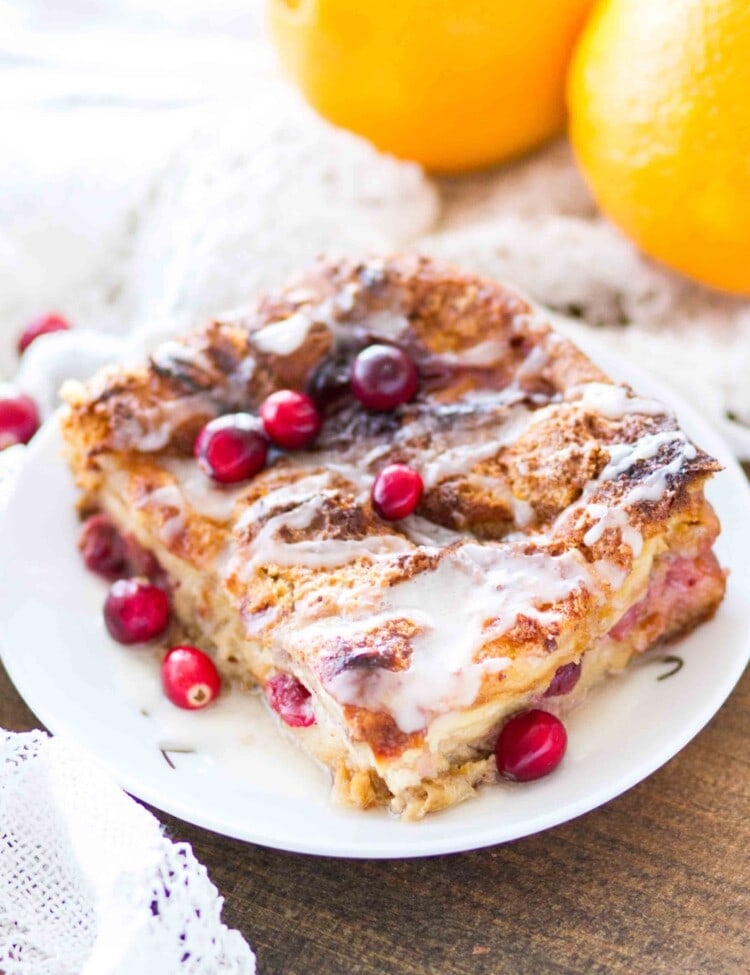 A large slice of cranberry orange bread pudding topped with icing on a white plate with cranberries