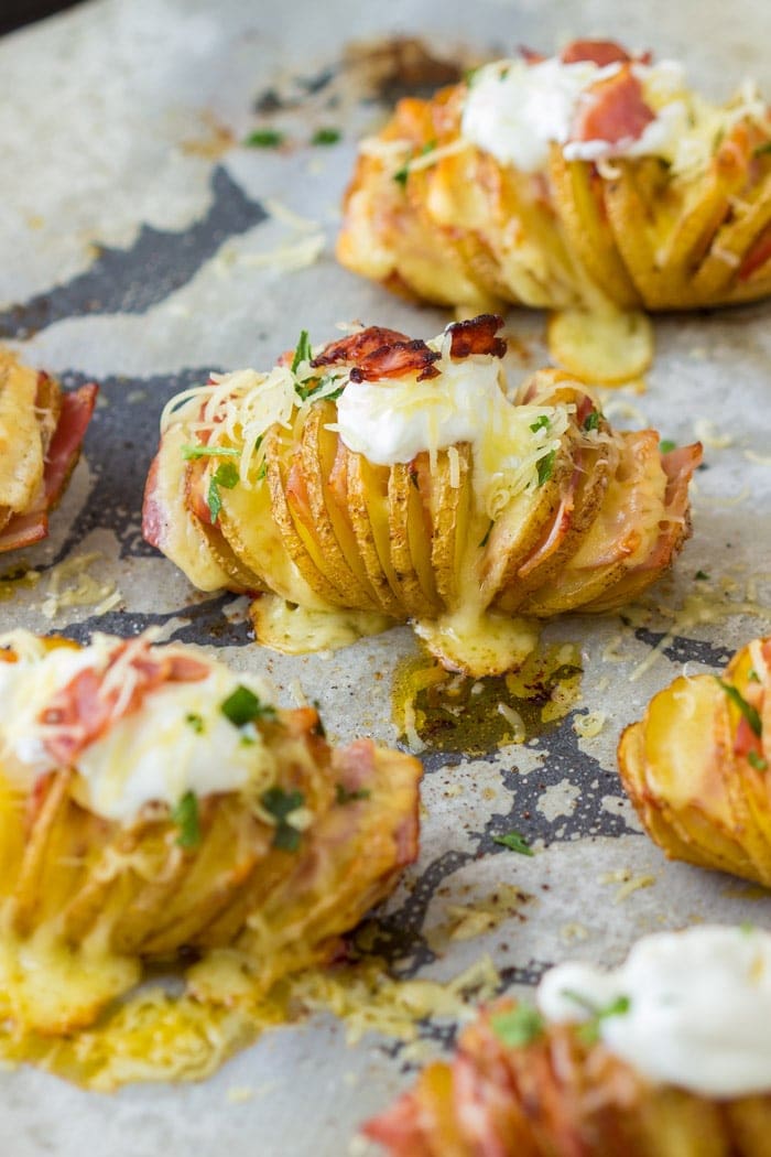 Wax paper with cooked hasselback potatoes on it topped with sour cream